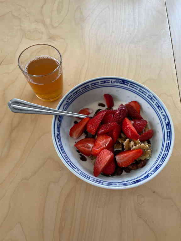A bowl of strawberry yoghurt and freshly cut strawberries with a glass of ice tea next to it.