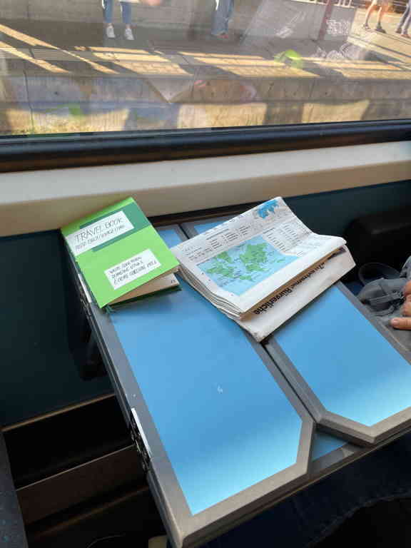 At the top left is the book I've created next to it is a newspaper. Both are placed on top of a small desk in a train.