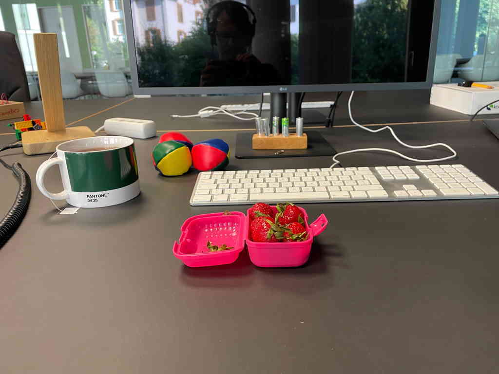 A clean desk with an Apple keyboard in the center and a pink box full of Strawberries in front. My tea mug is on the left of the keyboard. And behind the mug, you see the headphone stand I build a while ago.