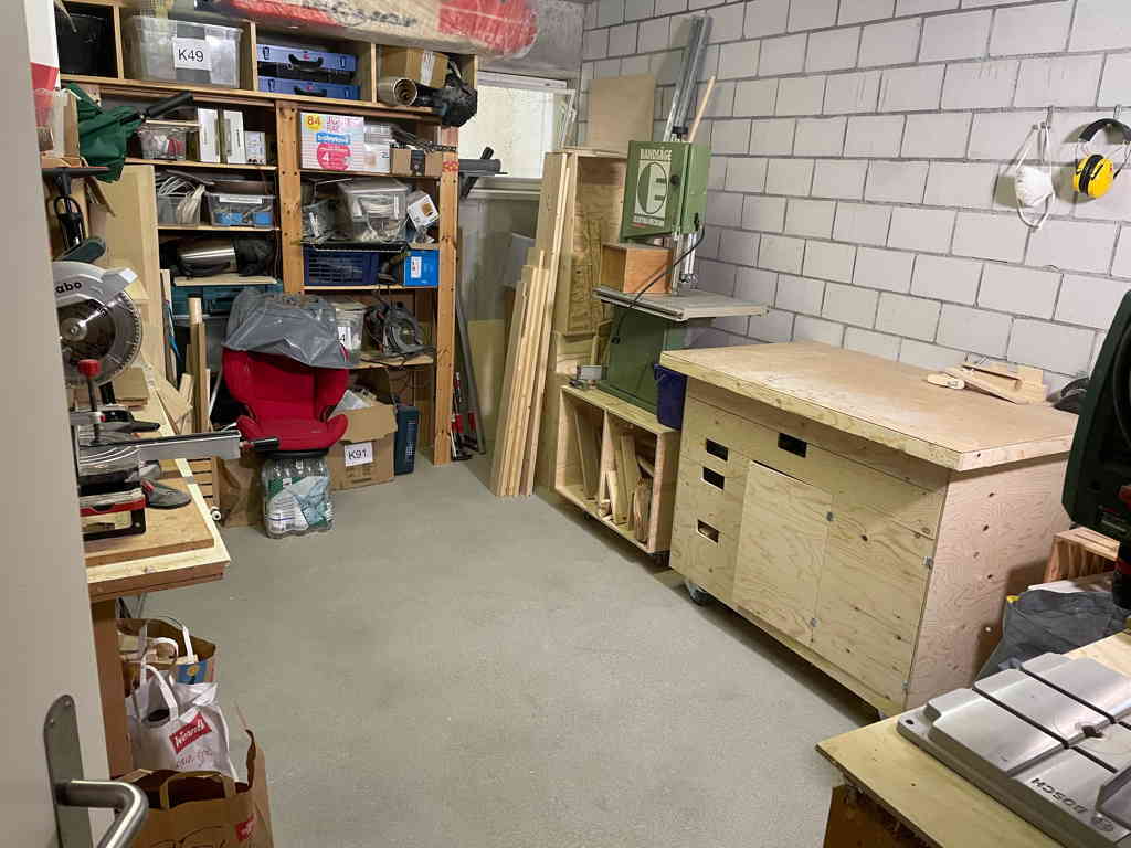 On the right side is my homemade workbench, next to it is the bandsaw. At the far end is a shelf with a lot of stuff. The image is taken from the door. The floor in the middle of the room is empty and clean.