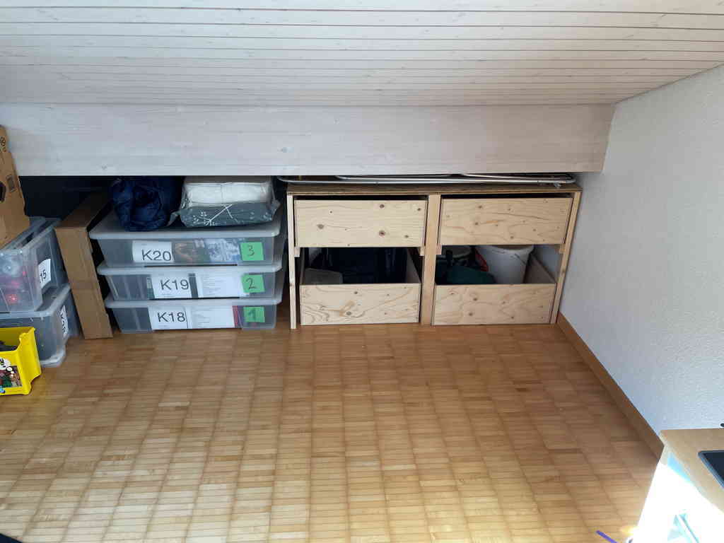 On the right side is a home built shelving unit with four drawers in it. The drawers are not yet full. Everything is pushed into outer most part of the room where the roof meets the floor. On the left of the unit are three boxes with our dvd collection.