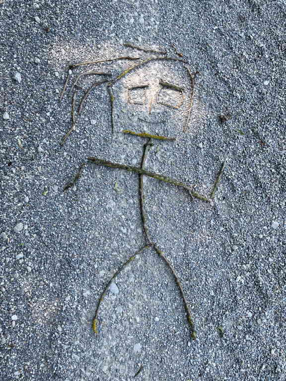 A stick figure made from short sticks I found by the way. The stick figure has a small and a square head, with long hair.