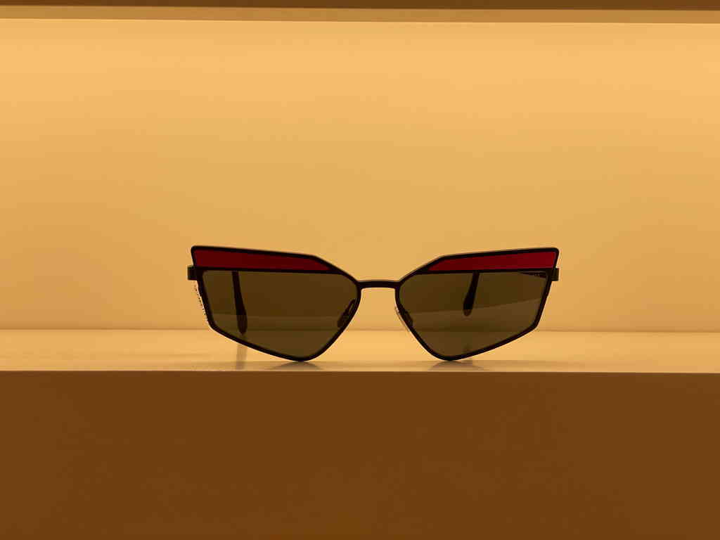 A pair of reading classes with a geometric shape and acute angles. The top part has a violet/pink color accent, which makes it look like you have violet/pink eyebrows. The image has bad lighting.