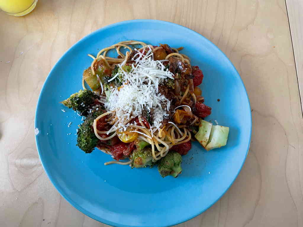 A plate with spaghetti, tomato sauce with broccoli and zucchini. With cheese on top.