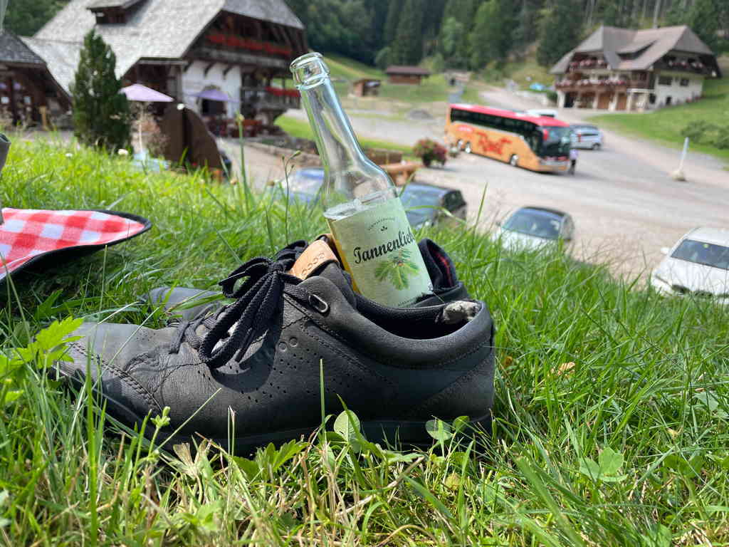 A bottle of Tannenliebe propped up inside on off my black boots. The boots stand on grass.