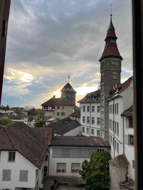 View out of the window showing two medieval towers. The closer one is round and has a point I roof. The farther one is square and a bit smaller.