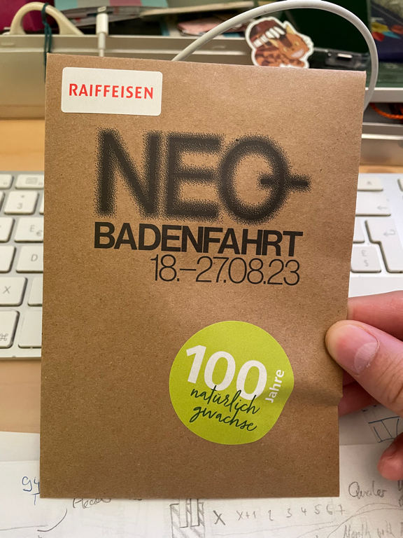 Zoomed-in picture of the Badenfahrt envelope containing the batch for entry. Text on the envelope reads: Raiffeisen (top left), NEQ BADENFAHRT 18.-27.08.23 (in the middle), 100 Jahre natürlich gewachsen (in a green circle / 100 years of natural growth)