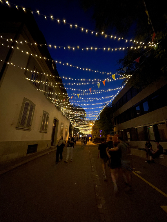 A night shot of string lights over a long street. The lights cross the street in a zig-zag-pattern.