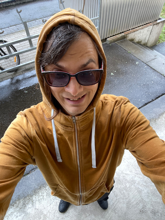 A selfie from the top downwards of me in a yellow hoody with sunglasses. Everything is wet. 