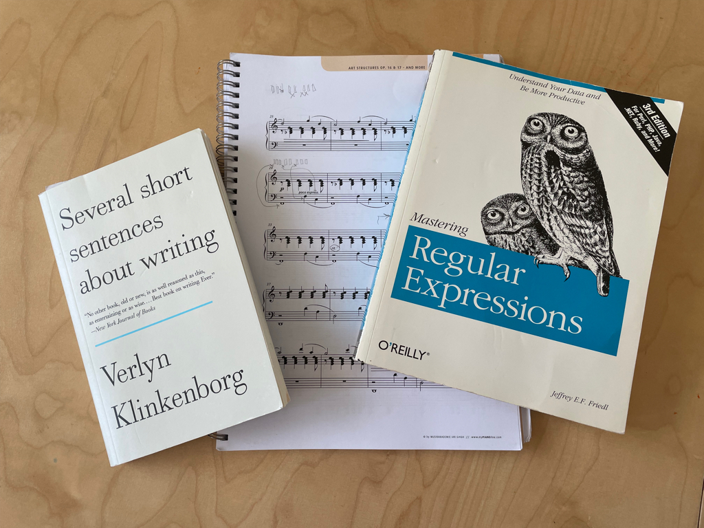 A close up photo of a collection of books. On the left is “Several short sentences about writing” by Verlyn Klinkenborg. On the right is “Mastering Regular Expressions” by Jeffrey E.F. Friedl. In the middle behind and partly covered by the other books, is my piano book with the current music pieces I’m working on.