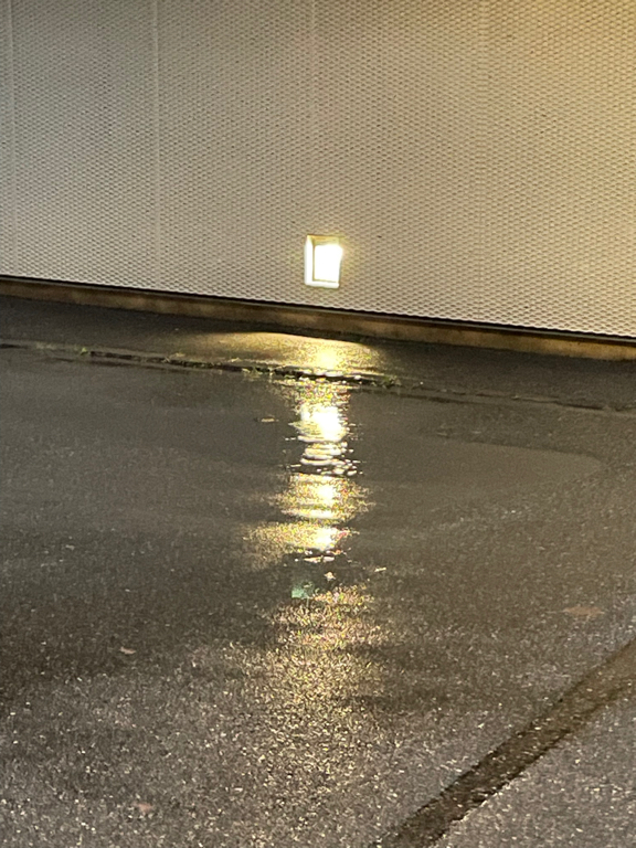 Close-up of an outdoor light reflecting in a rain puddle at the bottom.