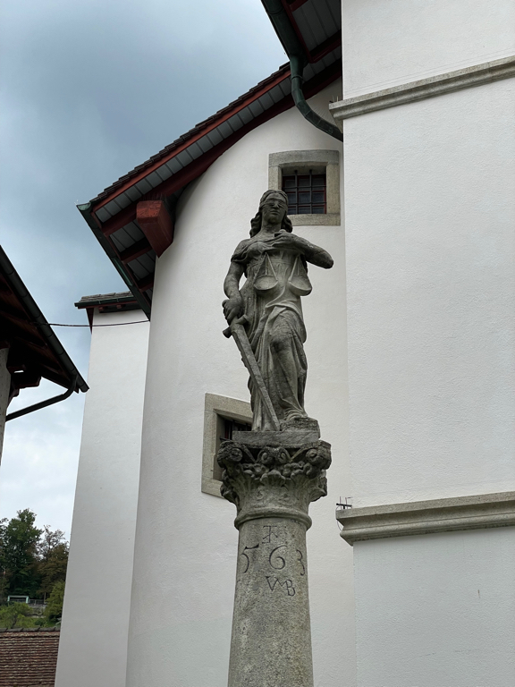 A zoomed-in photo of a statue on top of a fountain. The statue depicts the Justitia the goddess for justice.