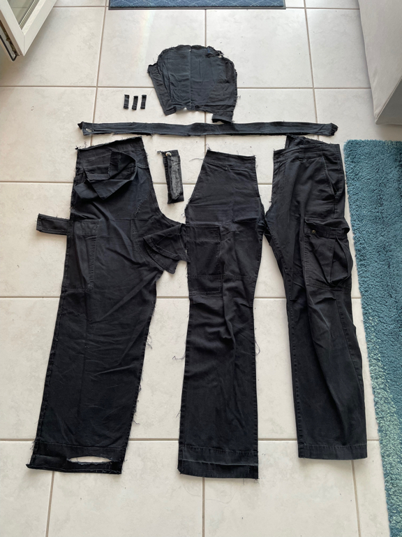 A zoomed-in photo of the parts of black pants. It looks like a sowing project and you are getting ready to sow the parts together again. On the left we have the first two parts of a leg and on the right is the other leg (still intact). On the top of the image are the smaller parts.