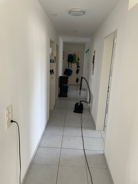 A picture of our hallway with the vacuum in the middle. And the crates for the dirty laundry in the back. The floors is white tile and the walls are white as well.