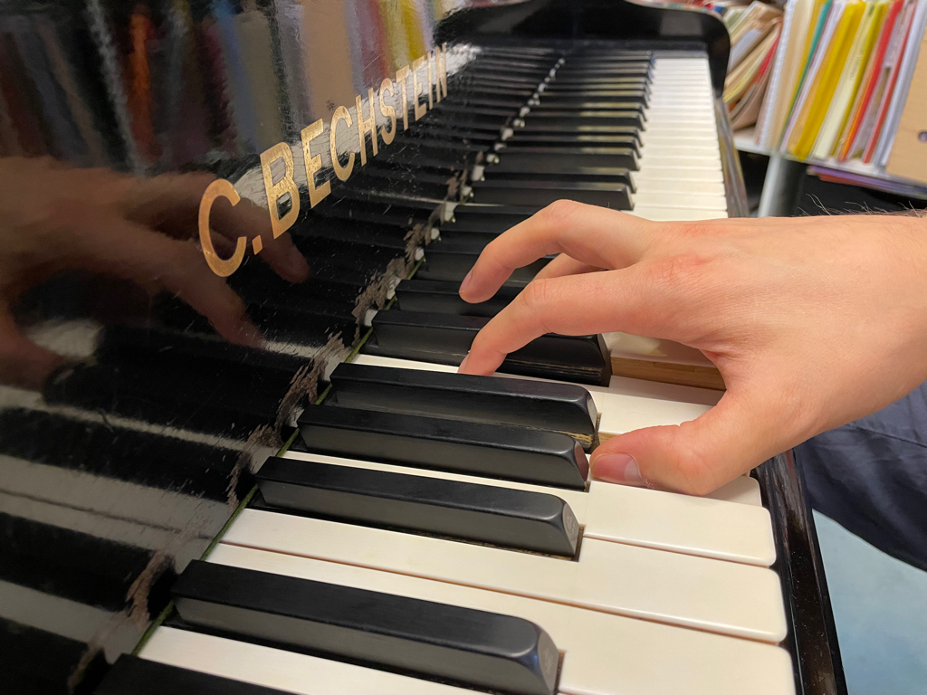 A close-up of my hand on a piano, trying to hold me fingers in the correct position. The text on the Piano reads “C. Bechstein” in all uppercase letters.