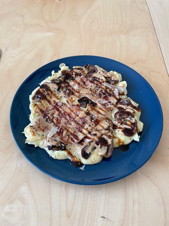 A close up of an Okonomiyaki on a blue plate on our kitchen table.