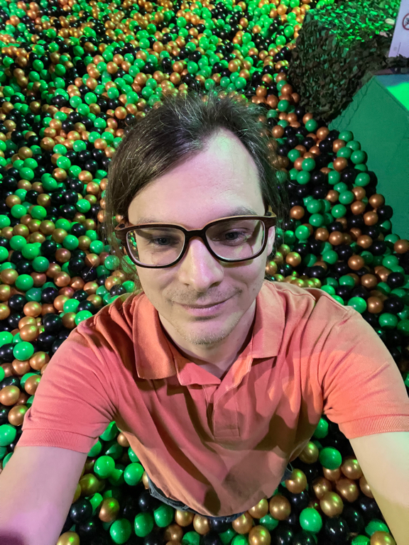 A selfie of me inside of a ball pool. I'm wearing my orange polo shirt. The picture is from high up so my whole body and part of the pool are visible.