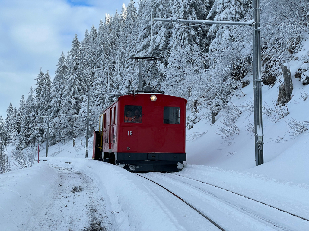 A wide shot of a red locomotive riding down the mountain in winter landscape.