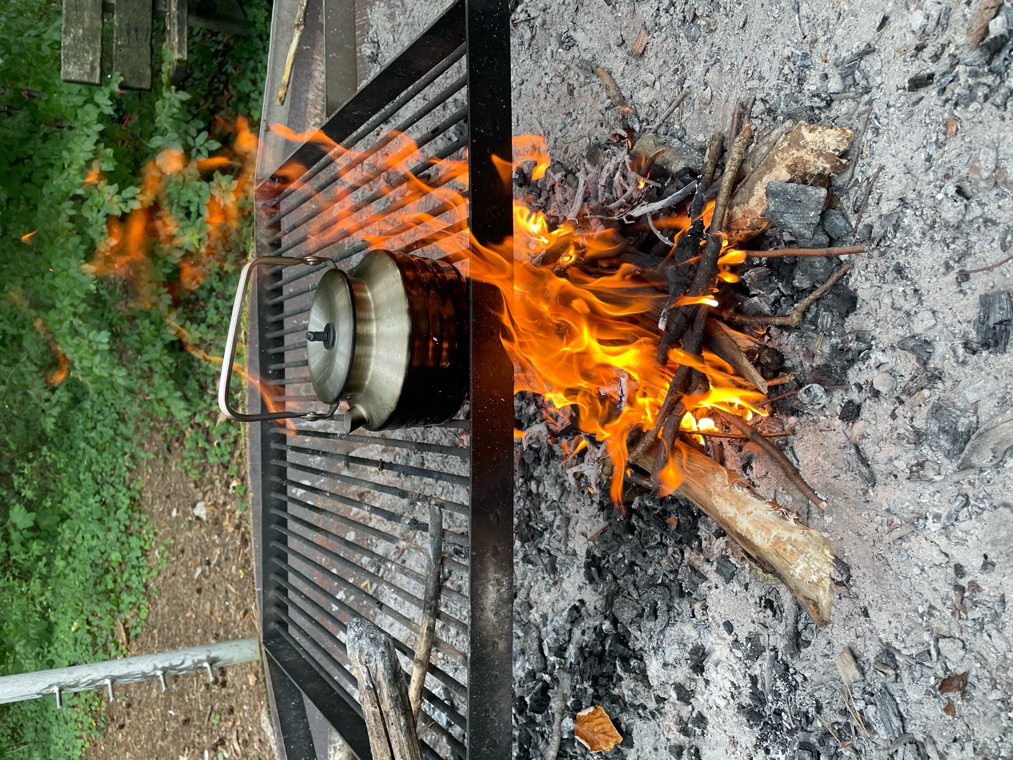 A wider shot of a roaring fire. The tea kettle is on top of a grill.