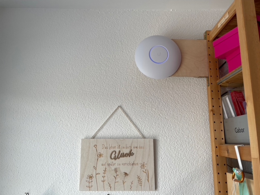 The final result with the installed access point in the top right. Hanging from a wooden IKEA shelf. Below it is an image with German Text about luck (“Das Lebel ist zu Kurt um das Glück auf später zu verschieben”).