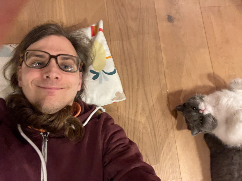 Selfie with me lying on the ground. I’m on the left side of the picture looking into the camera and Spacy (the cat) is on the left side also looking into the camera.
