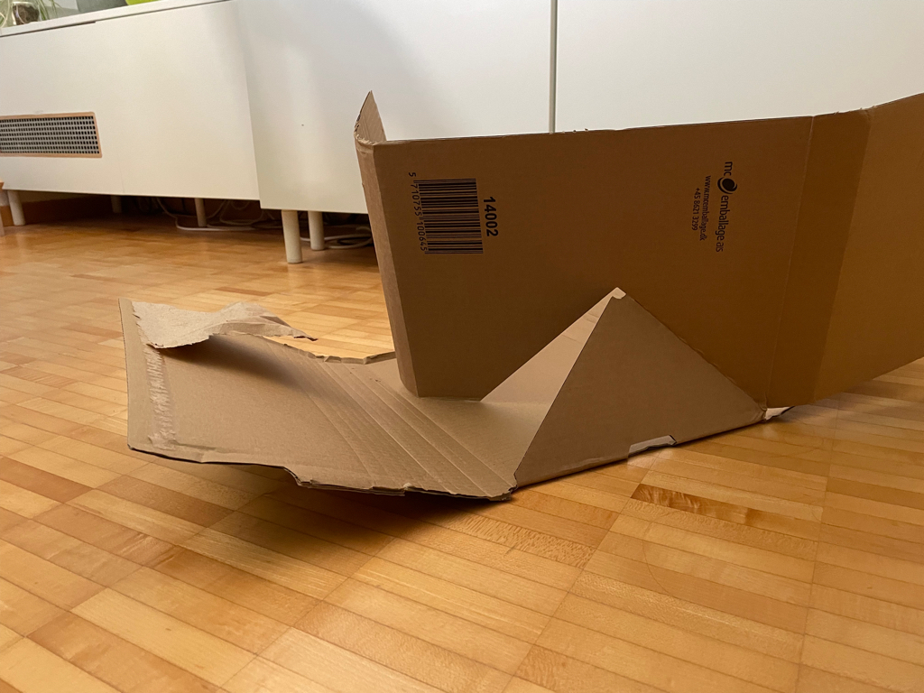 A close-up photo of a cardboard box. The triangular cut allows the second half to rotate by 90 degrees to form a box. This box was used to package books.