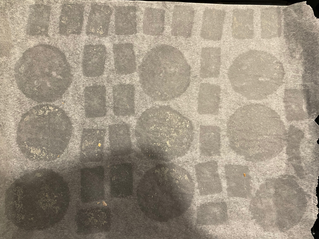 An empty cookie sheet with the outlines of the cookies embedded into the paper. The cookies were round and rectangular. In the bottom left corner is a bit of shadow.
