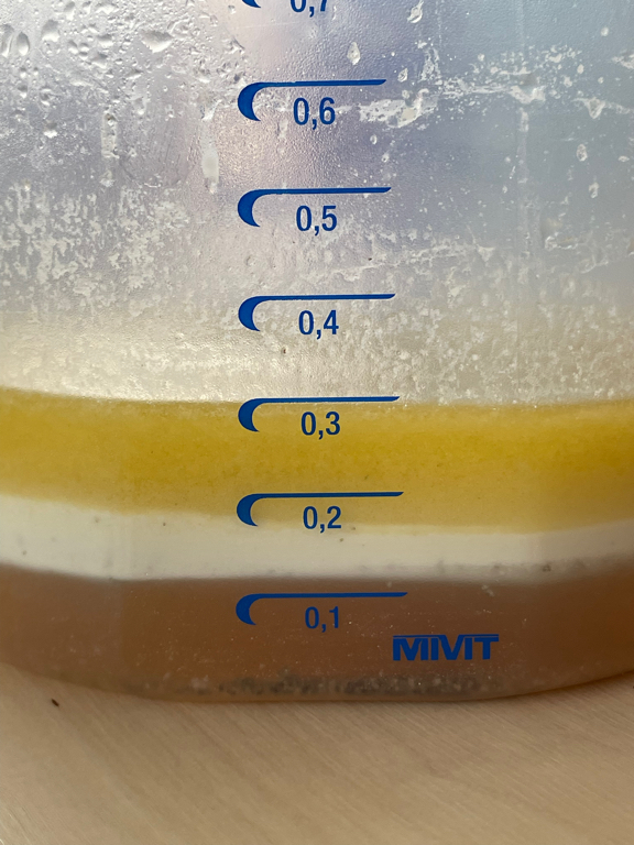 A closeup picture of a measuring cup with salad sauce.  The ingredients are split into three layers. Dark yellow oil on the top. Mayonnaise in the middle. And the vinegar (light brown) at the bottom. The measuring cup has a scale printed in blue on it. And the volume reads 0.2 liters in total.