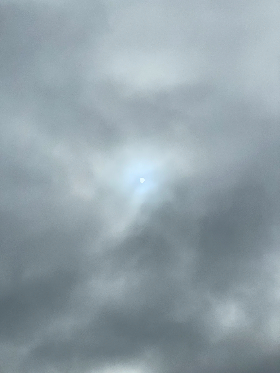 The image shows a cloudy sky with the sun faintly visible behind the gray clouds, casting a muted glow.