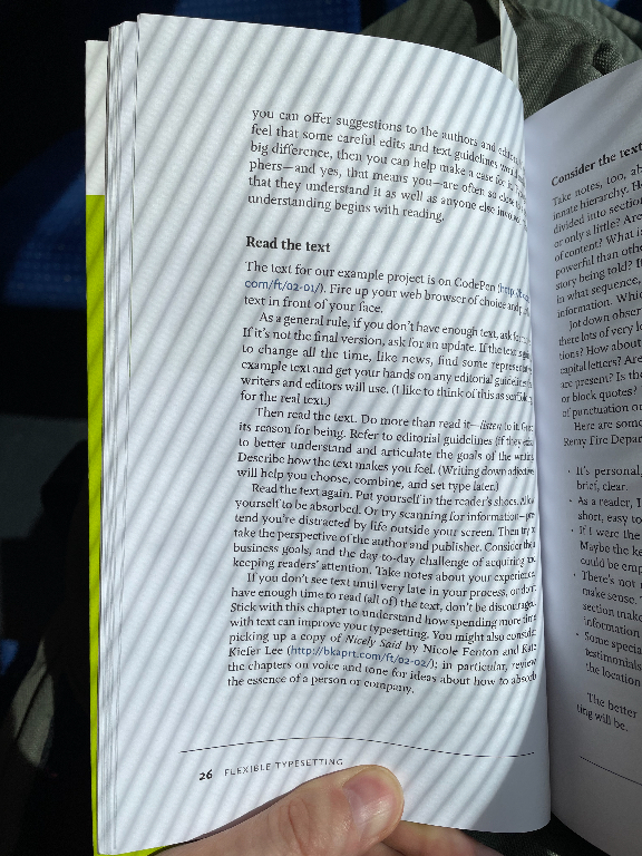 A person is holding an open book, with the pages text visible. The content includes headings and paragraphs, with visible lines of text. The lighting casts diagonal striped shadows over the pages, giving the image a textured appearance. The page number "26" is visible at the bottom of the left page, along with the words "FLEXIBLE TYPES," appearing to indicate a section or chapter in the book.