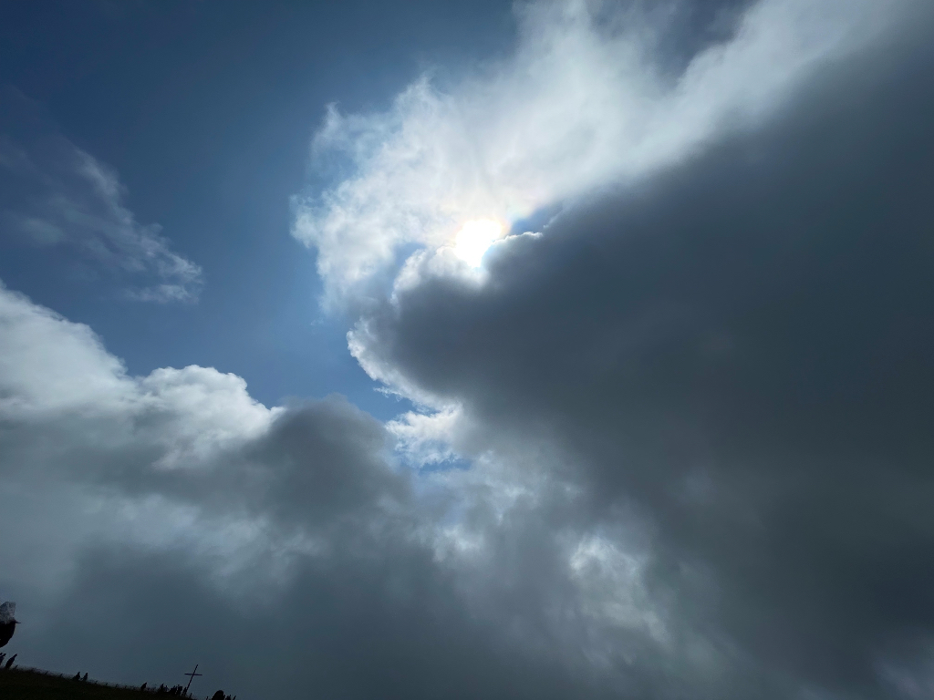 A dramatic sky with dark storm clouds partially covering the sun. The sun's rays create a bright spot in the otherwise cloudy scene, with patches of blue sky visible around the edges. The lighting gives a sense of a powerful and dynamic weather change.